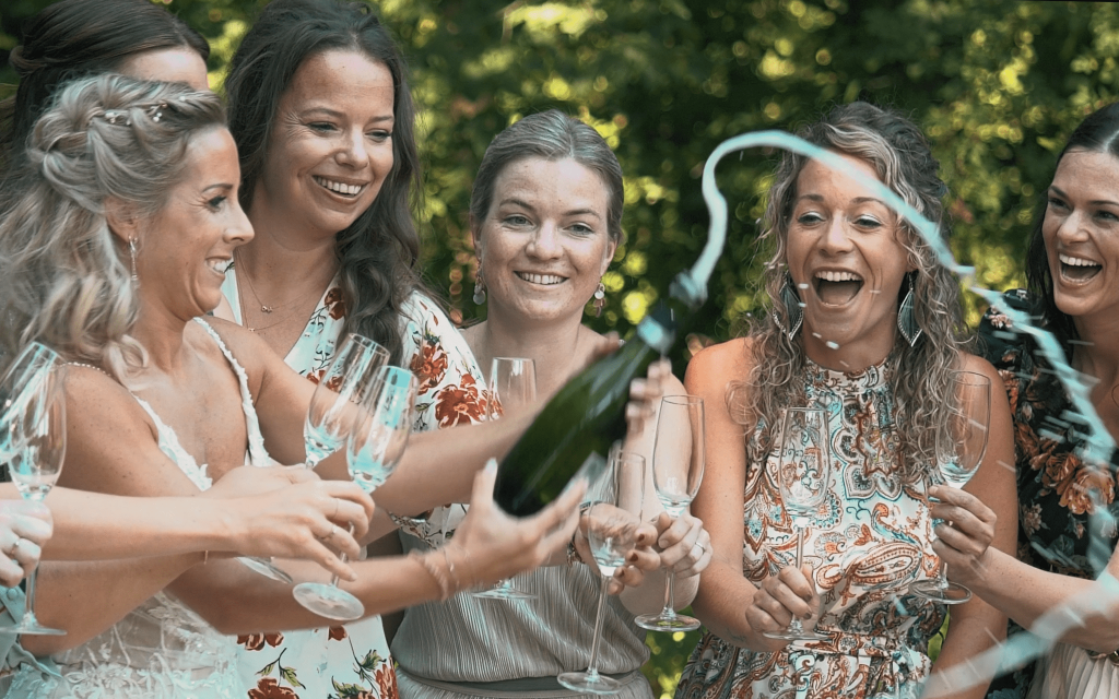 Groep vrouwen proost met champagne in tuin.