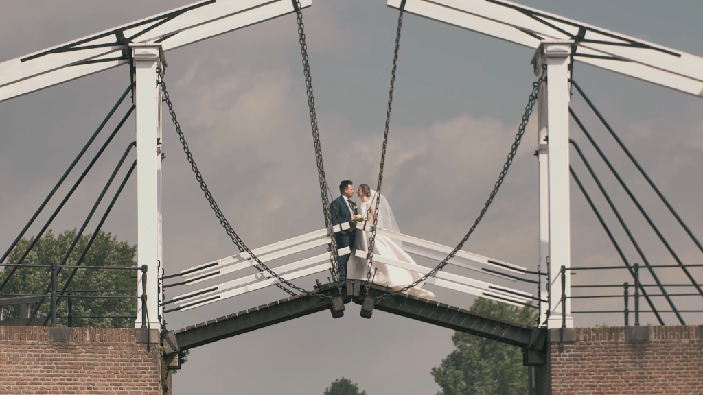 Bruidspaar op een ophaalbrug bij bewolkte lucht.